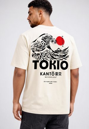 Mann trägt cremefarbenes T-Shirt mit schwarzer und roter Grafik einer stilisierten Ozeanwelle, roter Sonne und dem Schriftzug Tokyo auf dem Rücken.