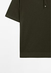 Polo shirt in verde oliva scuro con una finitura testurizzata, con maniche corte e orlo a coste. Include una patta con due bottoni.