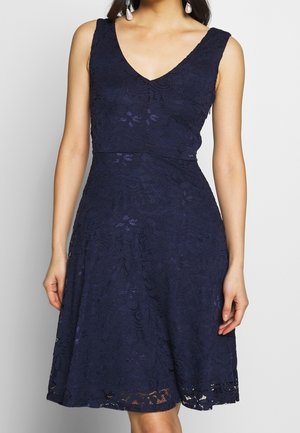 Vestido de encaje azul marino con escote en V, diseño sin mangas, cuerpo ajustado, falda acampanada y patrón floral, con un dobladillo con borde festoneado.