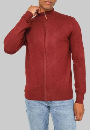 Pull zip rouge bordeaux avec un col montant, des poignets et un ourlet côtelés. Fabriqué en tissu tricoté texturé, avec une tirette en bois.