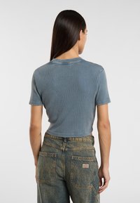 T-shirt a maniche corte di colore azzurro chiaro con scollatura rotonda, abbinato a jeans in denim strappati a vita alta con tasche posteriori.