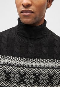 Čierny rolákový sveter s textúrou pleteného vrkoča a geometrickým strieborným a sivým vzorom na spodku. Mäkká, pletená tkanina.