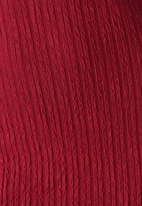 Punane tekstuuriga kangas, millel on vertikaalsed lainelised sooned, andes ruumilise välimuse. Pind on sile ja kergelt läikiv.