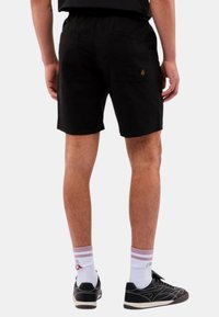 Svarta shorts med elastisk midja och två bakfickor. Bärs med vita strumpor med rosa ränder och svarta sneakers.
