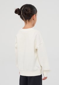 Felpa color crema con vestibilità ampia, spalle scese e polsini a coste. Texture morbida, senza motivi o hardware visibili.