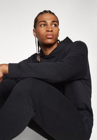 Zwarte hoodie met een zachte, gladde textuur; gecombineerd met bijpassende broek. Heeft een relaxte pasvorm en subtiele ontwerpelementen.