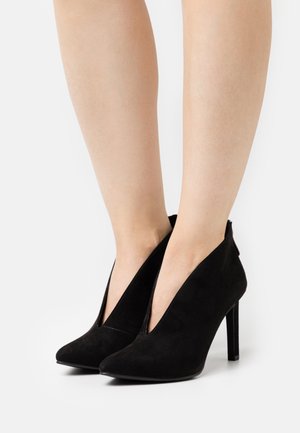 Black suede high-heeled shoes with a pointed toe and cut-out sides. Features a stiletto heel and smooth texture.