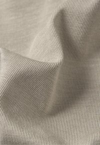 Beżowa tkanina o fakturze z delikatnym prążkowanym wzorem, ukazująca miękkie fałdy i lekki połysk. Materiał wydaje się lekki i elastyczny.