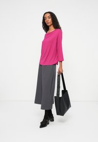 Fuksjowa bluzka z drapowanym dekoltem, rękawami trzyczwartowymi; szare spodnie w szerokim kroju; czarna torba z paskiem; czarne buty na obcasie.