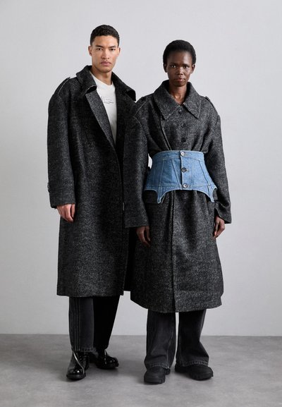 Abrigos oscuros de gran tamaño con textura de espiga, que cuentan con grandes cuellos y botones. El segundo modelo lleva un cinturón corsé de denim azul.