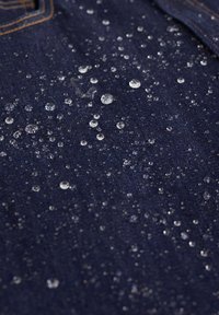 Vodoodbojna temno modra denim tkanina z številnimi prozornimi kapljicami vode razpršenimi po površini, ki poudarjajo njeno teksturo.