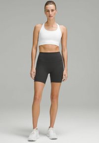 White sports bra and high-waisted black shorts, both made of stretchy fabric. Model wears white athletic shoes. Simple design, no patterns.