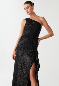 Crna večernja haljina na jedno rame s aplikacijama od sekvenci, bočnim prorezom i drapiranim detaljima; elegantan, tijelu prilagođen dizajn.