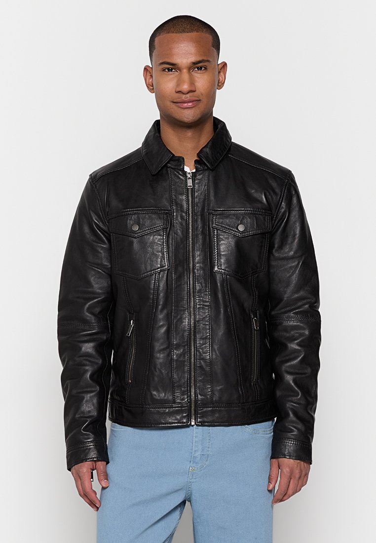 Giacca di pelle nera con due tasche sul petto, chiusura zip e maniche lunghe. Presenta un colletto e una superficie liscia, leggermente lucida.
