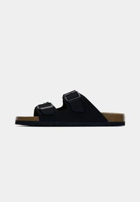 Μαύρο σουέντ σανδάλι με δύο ρυθμιζόμενους ιμάντες με αγκράφες, φυσική φαρδιά σόλα φελλού και υφασμένο λαστιχένιο πέλμα. Πλάγια όψη.