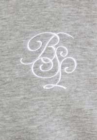 Initiales brodées blanches ornées « BSP » sur un fond de tissu gris clair et doux.
