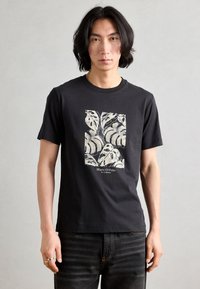 T-shirt nera in cotone con una grafica color crema di foglie tropicali e il testo "Marc O'Polo" in basso. Design a maniche corte e collo rotondo.