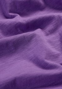 Tela púrpura con una superficie suave y texturizada y un ligero brillo, que muestra pliegues suaves y un tejido liso y uniforme.