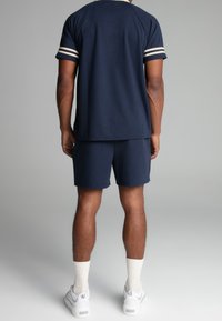 Navy short-sleeve t-shirt with white and gold stripes on the sleeves, paired with matching shorts. Worn with white sneakers and textured socks.
