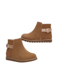 Botas de tobillo de ante color beige con un acabado texturizado, que cuentan con una correa brillante y un acento en forma de corazón en el talón. Suela de goma para agarre.