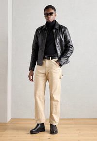 Μαύρο δερμάτινο μπουφάν πάνω από μαύρο ζιβάγκο, συνδυασμένο με μπεζ παντελόνι και μαύρες μπότες μέχρι τον αστράγαλο. Αξεσουάρ περιλαμβάνουν γυαλιά ηλίου και ζώνη.