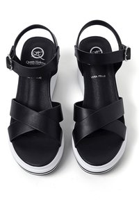Sandali platform in pelle nera con fasce incrociate, fibbia alla caviglia regolabile e suola bianca. Insole texturizzato, realizzati in "vera pelle."