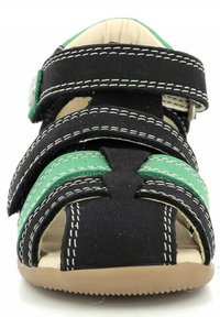 Chanclas negras y verdes que cuentan con correas ajustables con costuras blancas, diseño de punta abierta y suela de goma color marrón.