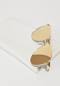 Occhiali da sole aviator color oro con lenti marroni sfumate in una custodia bianca testurizzata impreziosita dalla scritta "Le Specs."