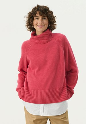 Roze trui met een hoge geribde col, relaxed fit, geribde onderrand en manchetten, gedragen over een wit shirt, weergegeven tegen een effen achtergrond.