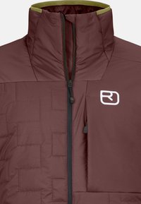 Burgundy insulated jacket with a high collar, zip closure, side pocket, and contrasting green neckline; features quilted texture and logo.