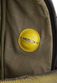 Interior de tela verde con un acento redondo de cuero amarillo con una hendidura, revelando un inserto de metal. Patrón texturizado visible en el fondo.