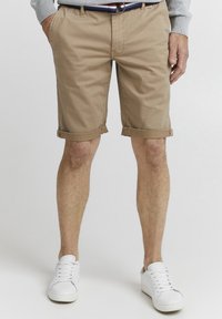Kaki bomullshorts med rullekanter, sidelommer og belte. Kombinert med hvite sneakers. Flat front og uformell design.