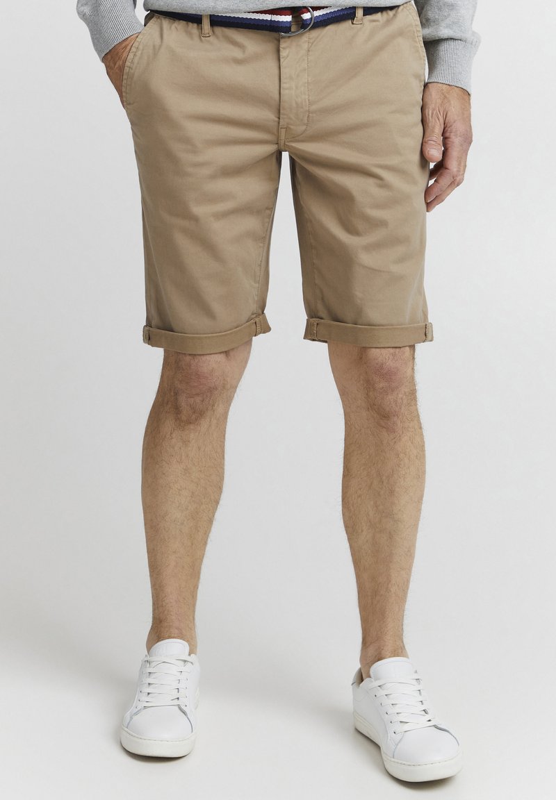 Kaki bomullshorts med rullekanter, sidelommer og belte. Kombinert med hvite sneakers. Flat front og uformell design.