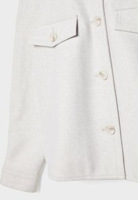Veste en laine gris clair avec une poche poitrine à rabat, fermeture à boutons et manches longues à poignets, montrée de la taille à la poitrine.