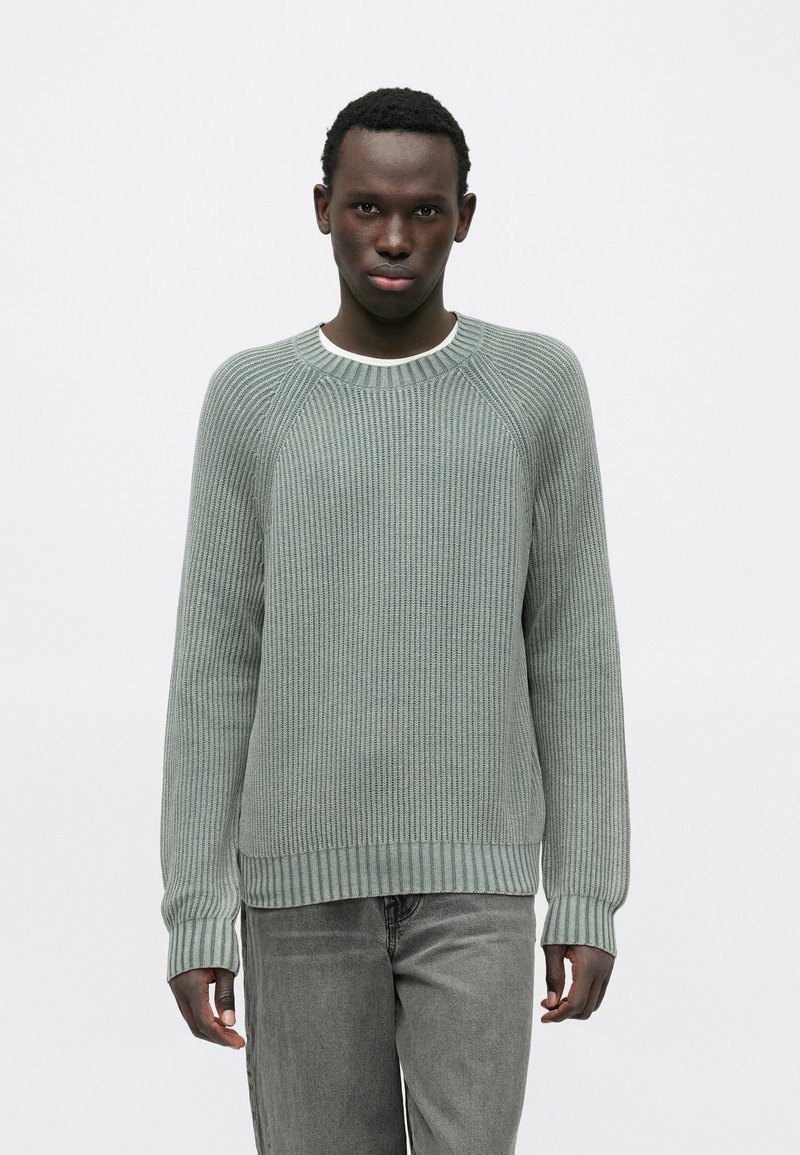 Gaiši zaļš ribots džemperis ar apaļu kakla izgriezumu un garām piedurknēm. Izceļas ar struktūr�ētu trikotāžu un ribām ap manšetēm un apakšmalu. Kombinēts ar pelēkām džinsu biksēm.