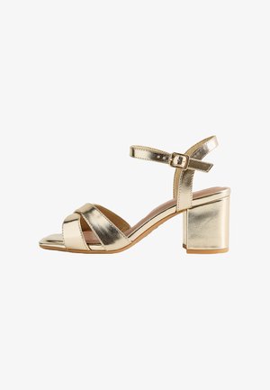 Sandalo metallizzato color oro con cinturini, tacco a blocco e fibbia regolabile alla caviglia, punta aperta e cinturini incrociati sul davanti.