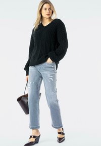 Suéter negro de punto con escote en V, con un diseño de trenzas texturizadas. Combinado con jeans desgastados de un azul claro y tacones tipo cuña negros.