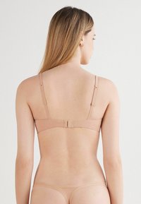 Podprsenka v tělové barvě s nastavitelnými ramínky, zapínáním na háček a oko na zadní straně a hladkým povrchem, navržena pro bezproblémové nošení.
