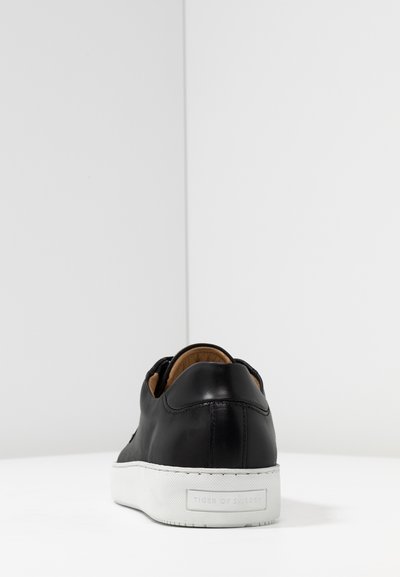 Sneaker in pelle nera con suola in gomma bianca, forma arrotondata, superficie liscia e dettaglio del logo sul tallone. Design casual adatto per l'uso quotidiano.
