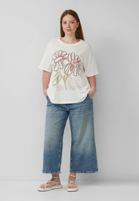 Losse crème t-shirt met bloemenprint in roze en bruin, gecombineerd met lichtblauwe wijde jeans en beige sandaaltjes met banden.