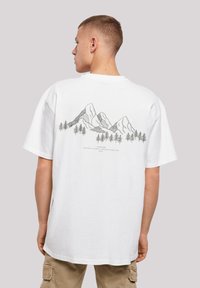 Witte katoenen T-shirt met een zwart grafisch ontwerp van een berg en boom op de achterkant. Korte mouwen en een losse pasvorm met een ronde hals.
