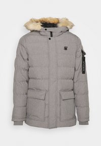 Graue Daunenjacke mit Kunstfellkapuze. Zu den Merkmalen gehören zwei vordere Taschen, eine Reißverschlusstasche am Arm und ein Logo. Strukturiertes Material mit Kammdesign.