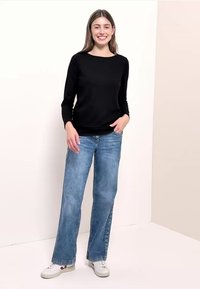 Top nero a maniche lunghe abbinato a jeans ampi color azzurro chiaro e sneaker bianche. Design semplice senza motivi o decorazioni visibili.