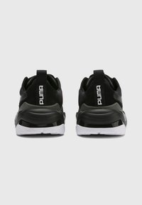 Czarne buty sportowe o smukłej sylwetce, z teksturowaną czarną cholewką, białą podeszwą oraz wyraźnym logo Puma na zakładce pięty.