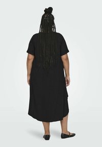 Robe noire mi-longue à manches courtes, au design simple, avec une coupe décontractée et une fente sur le côté. Des ballerines noires complètent la tenue.