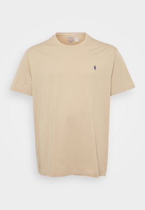 Beige bomullströja med rund hals, korta ärmar och en liten blå broderad logotyp på vänster bröst. Mjuk textur, avslappnad passform.