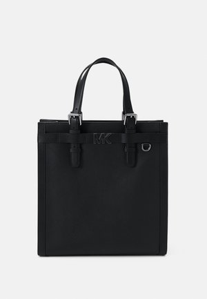 Sac cabas en cuir noir avec deux anses, boucles argentées, un petit anneau en métal et un logo "MK" centré à l'avant.