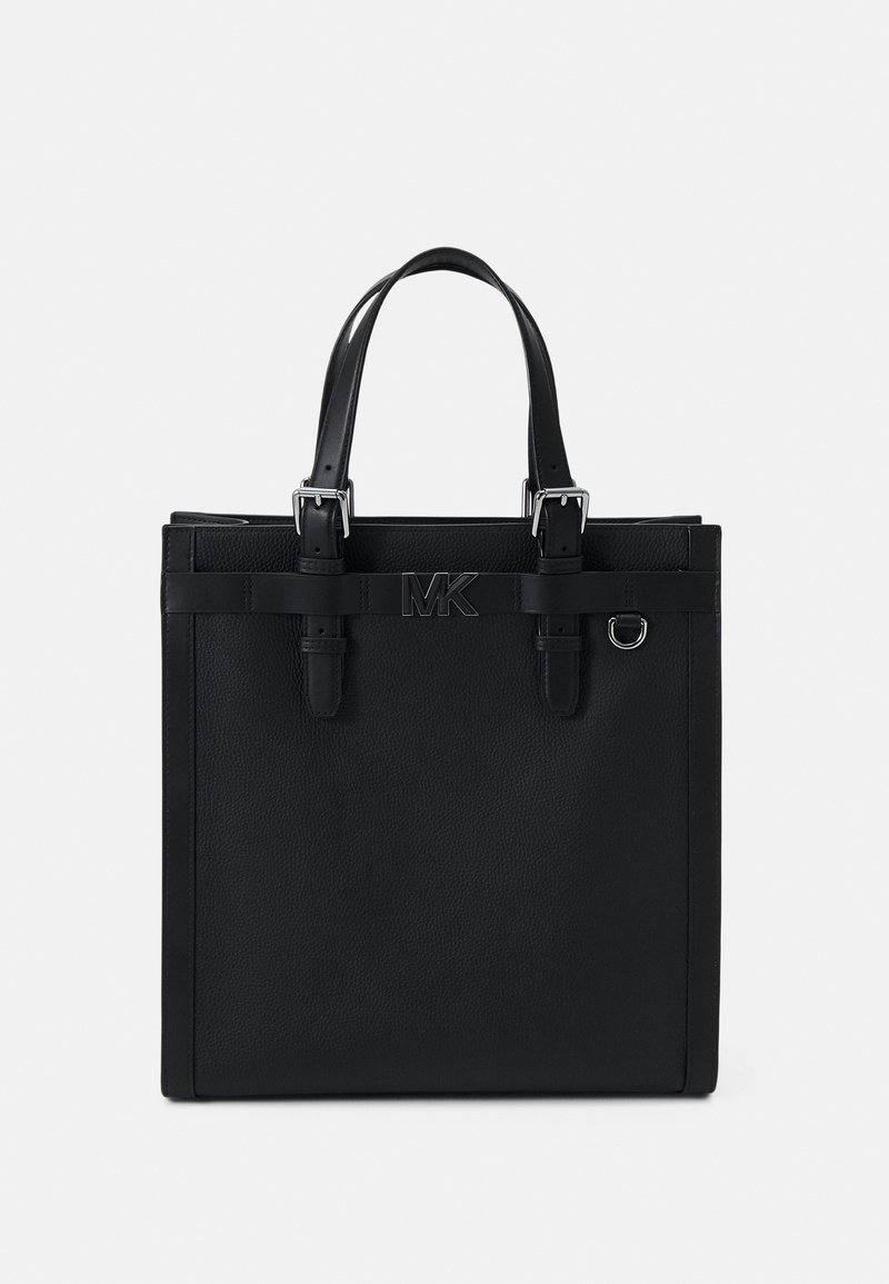 Sac cabas en cuir noir avec deux anses, boucles argentées, un petit anneau en métal et un logo "MK" centré à l'avant.