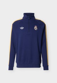 Marineblauer Sweatshirt mit Viertel-Reißverschluss, gelben Schulterstreifen, Adidas-Logo auf der linken Brust und Real-Madrid-Wappen auf der rechten Brust.