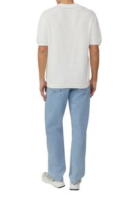Chemise blanche à manches courtes, en tricot texturé avec des rayures horizontales, associée à un jean bleu clair ample et des baskets blanches.